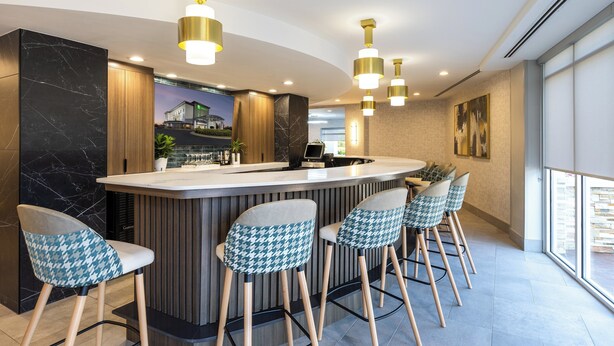 Un espace bar moderne avec un comptoir en marbre, des chaises à motifs pied-de-poule et des luminaires suspendus.
