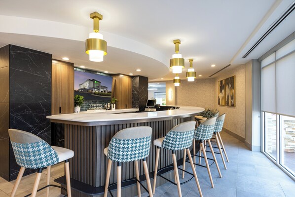 A modern bar area with a marble counter, houndstooth patterned chairs, and pendant lighting.