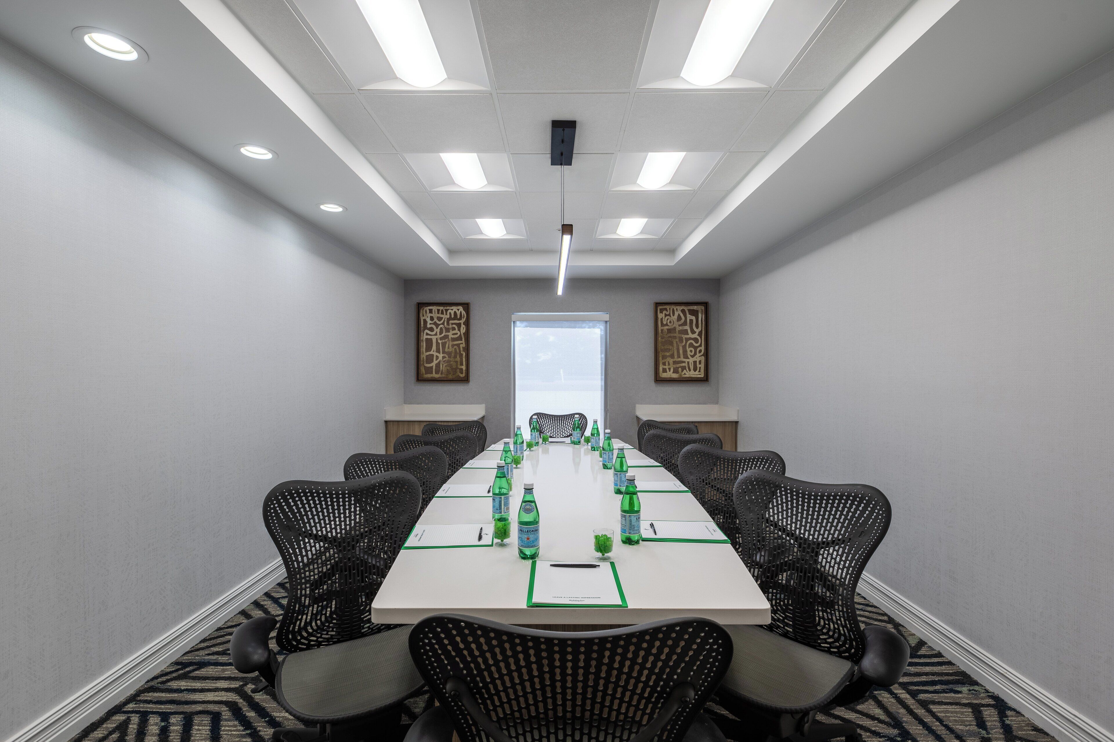 A conference room with a long table, black chairs, water bottles, and a projector screen.