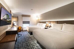 A hotel room with two beds, a desk, a chair, a TV, and a large window.
