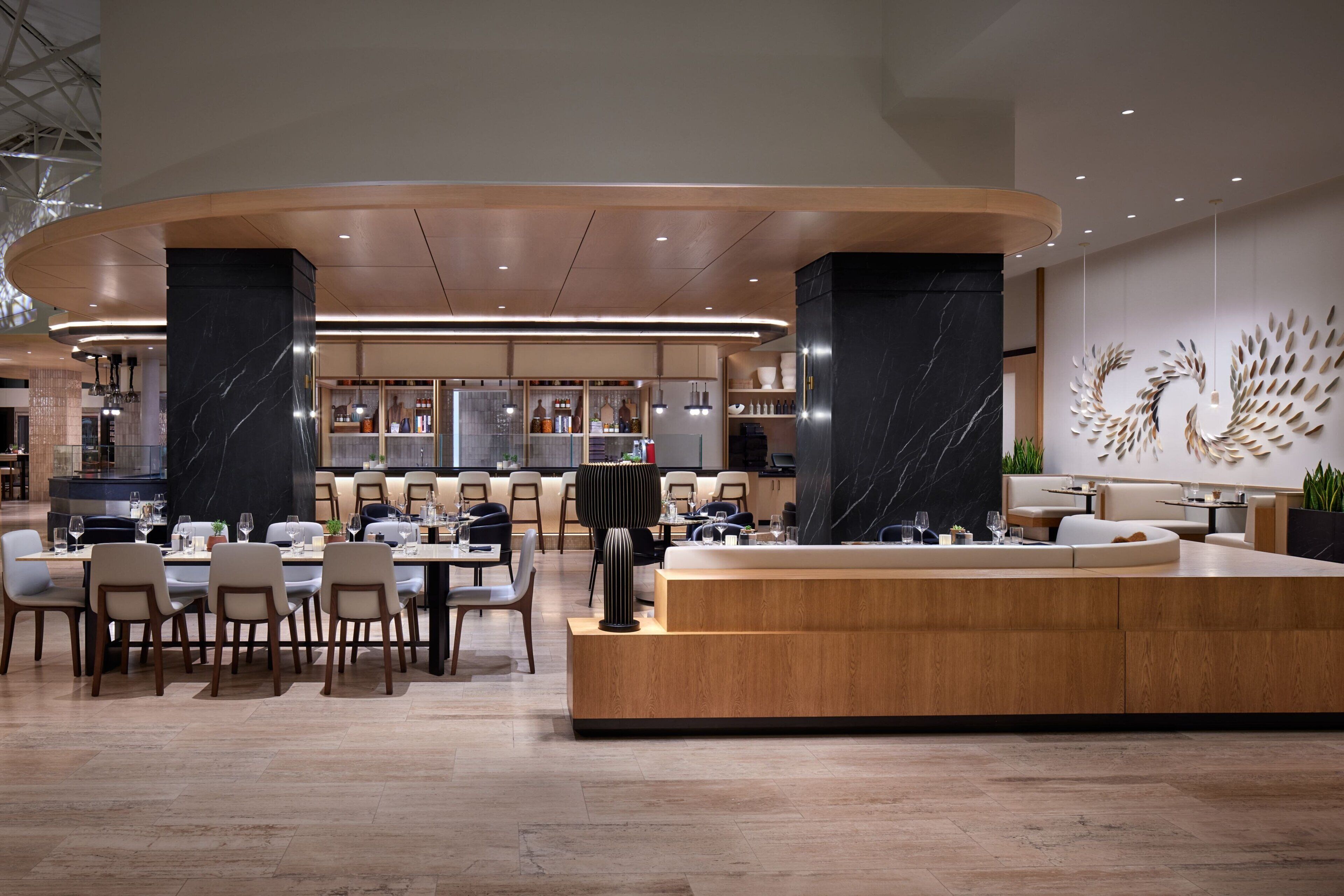 Un hall d’hôtel moderne avec un comptoir d’accueil central, des espaces de détente et un bar.