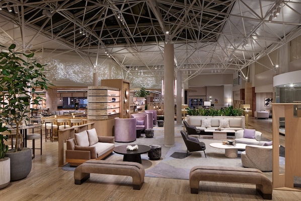 A spacious lobby with modern furniture, a high ceiling with a geometric design, and a large plant in the foreground.