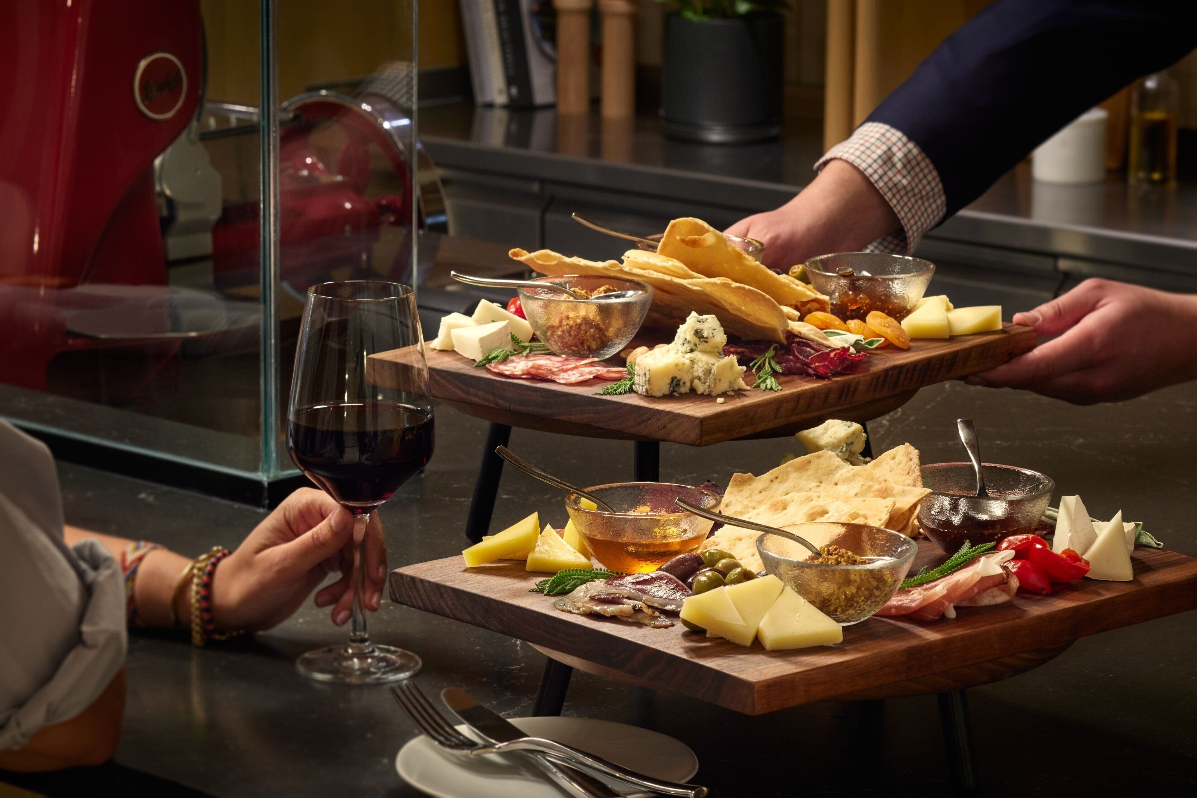 A wooden board with various cheeses, meats, and crackers, accompanied by a glass of red wine.