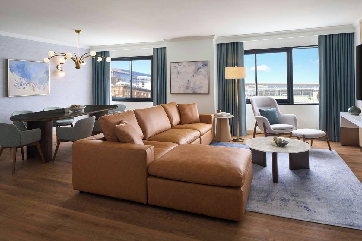 A modern living room with a sectional sofa, dining area, and large windows offering city views.