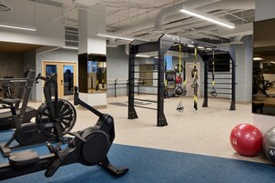 Une salle de sport équipée de divers appareils, notamment un tapis de course, un vélo d’appartement et une barre de traction.