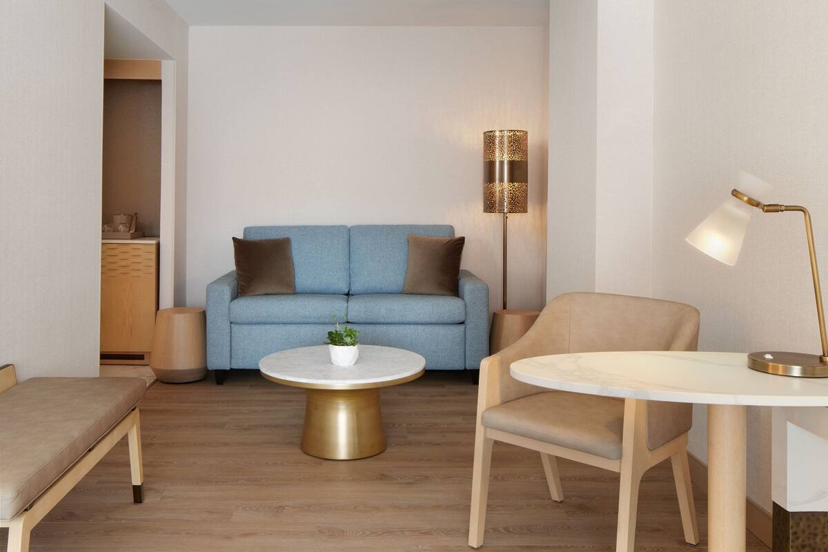A modern living room with a blue sofa, a round coffee table, a beige armchair, and a floor lamp.