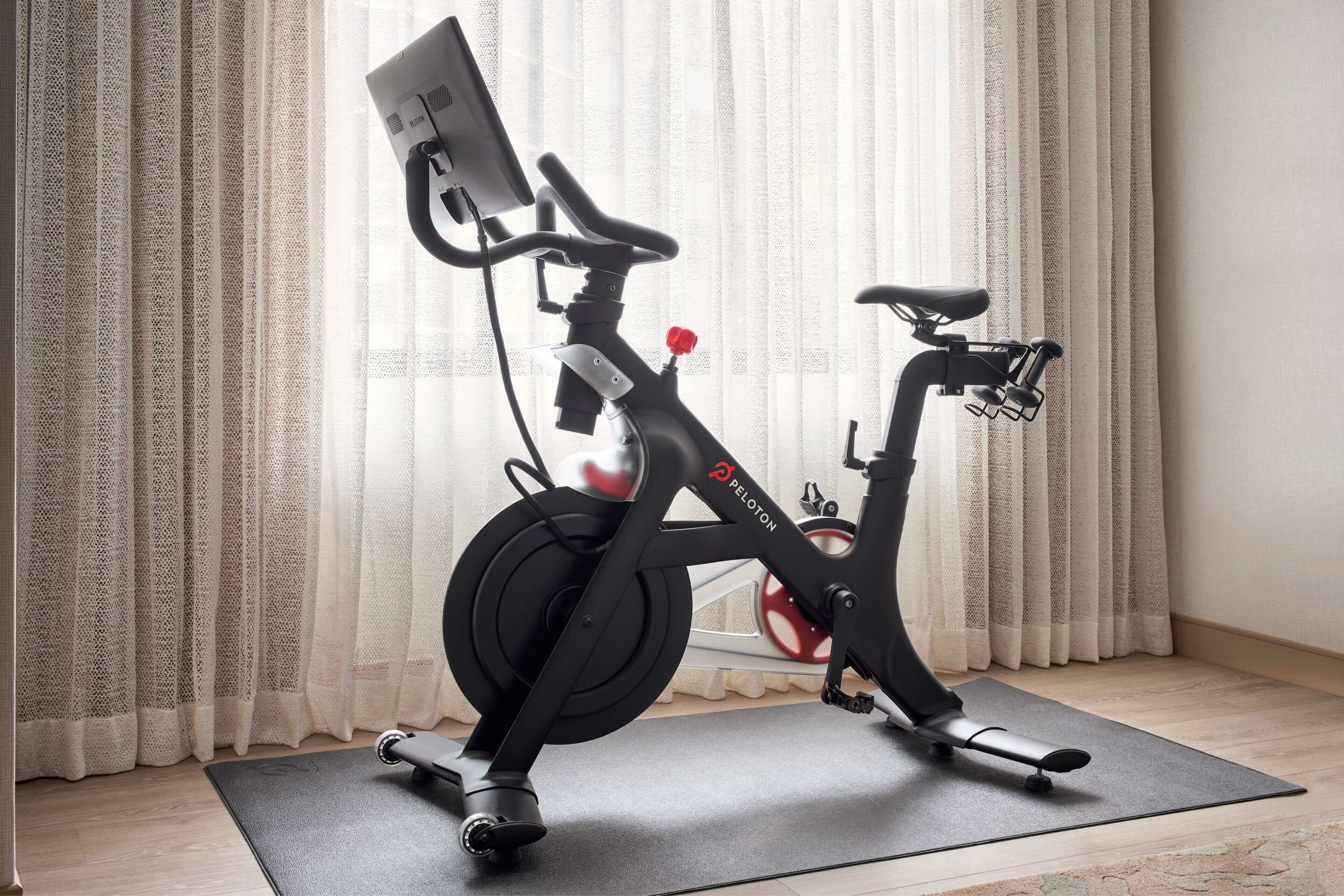 A stationary bike in a room with a curtain, a mat, and a wall-mounted device.
