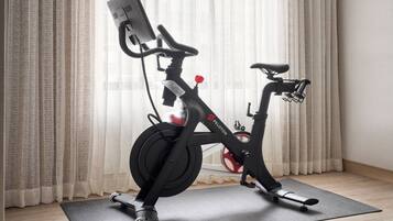 A stationary bike in a room with a curtain, a mat, and a wall-mounted device.