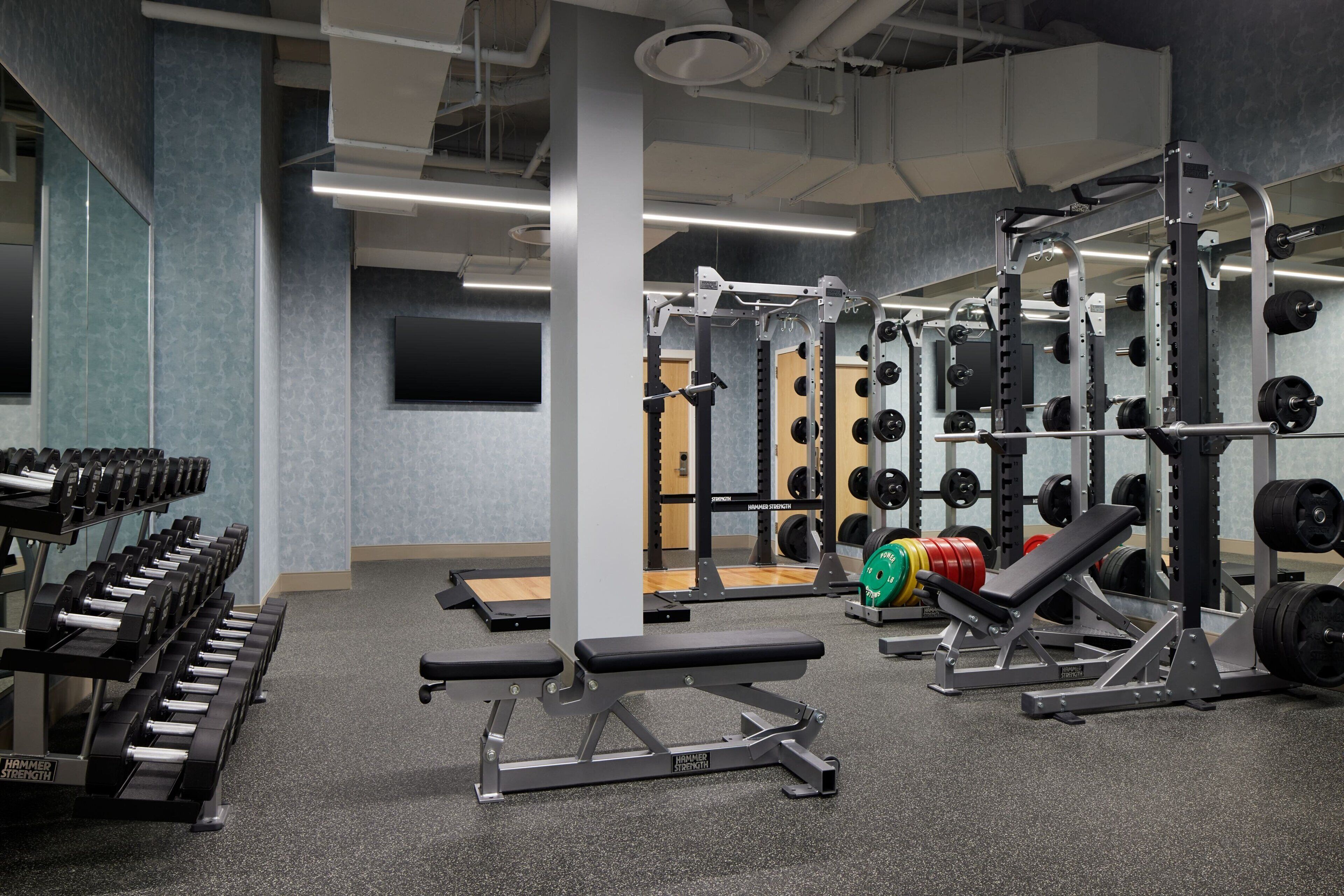 A gym with weightlifting equipment, benches, and a wall-mounted TV.