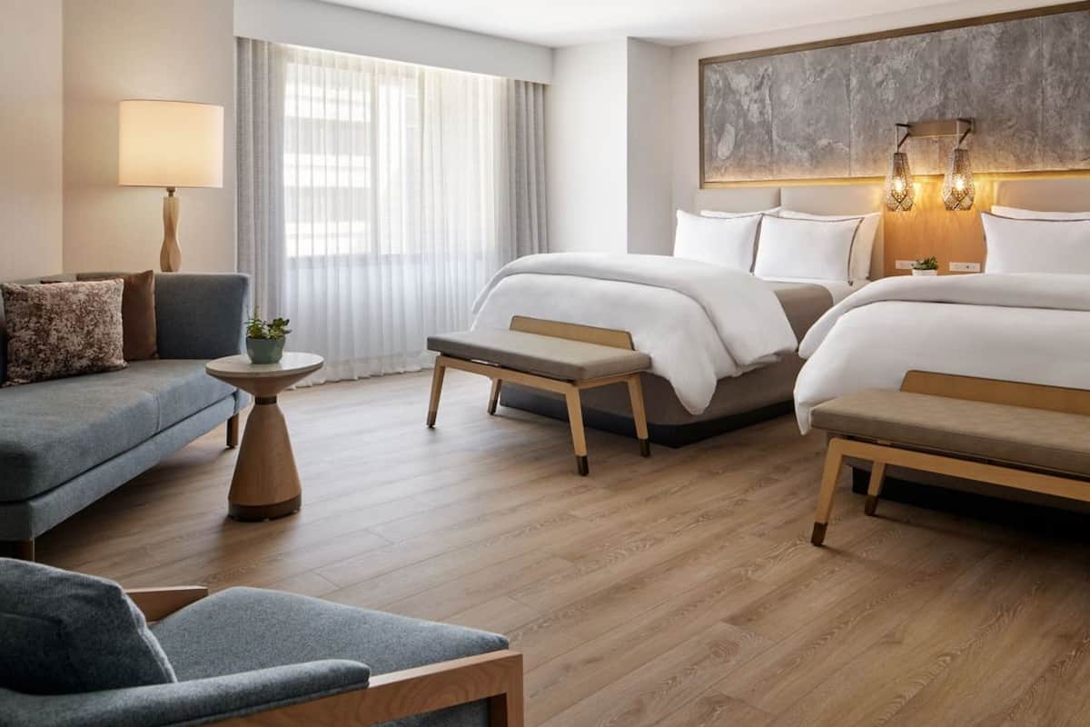 A hotel room with two beds, a sofa, a small table, and a bench.