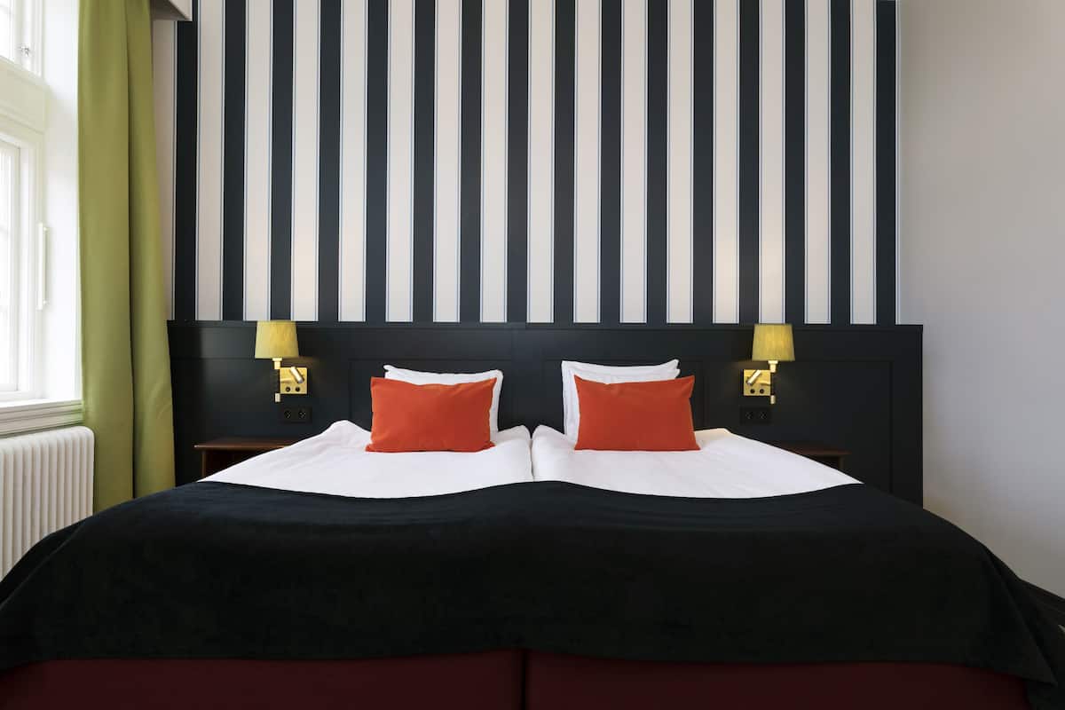 A double bed with a black and red bedspread, two red pillows, and a striped headboard.