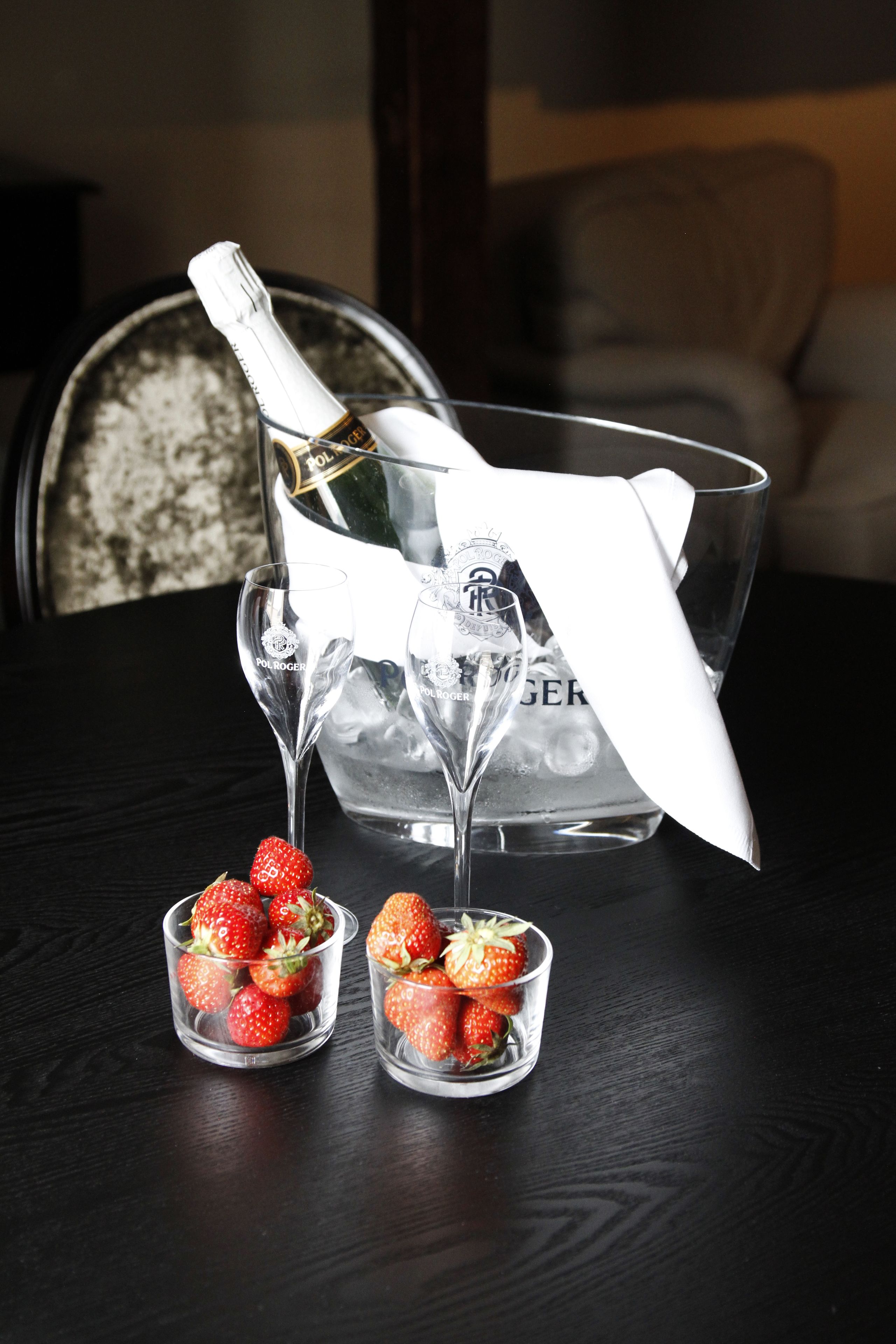 A bottle of champagne, two glasses, and two small glasses with strawberries on a dark wooden table.