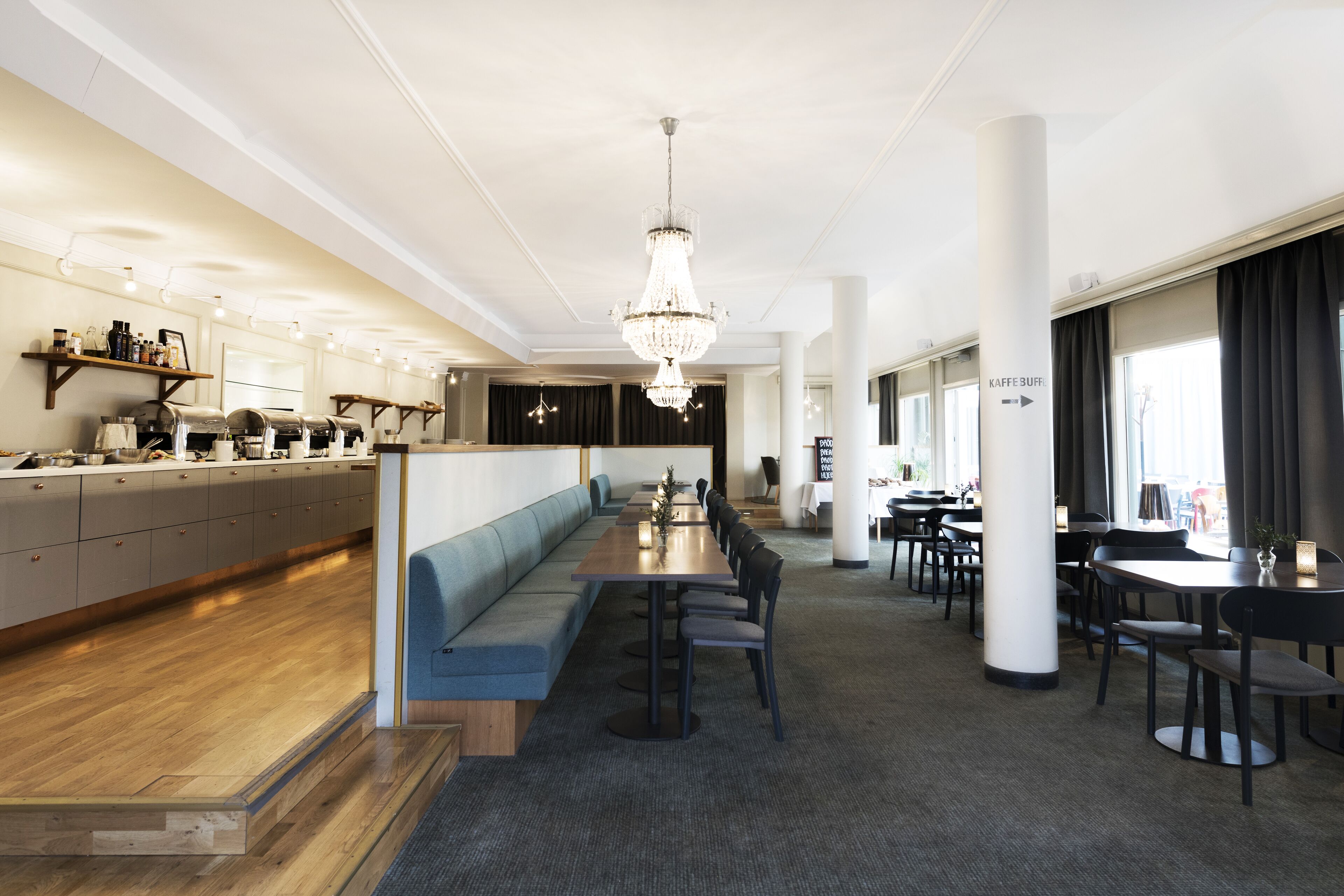 A modern hotel lobby with a long counter, seating area, and a chandelier.