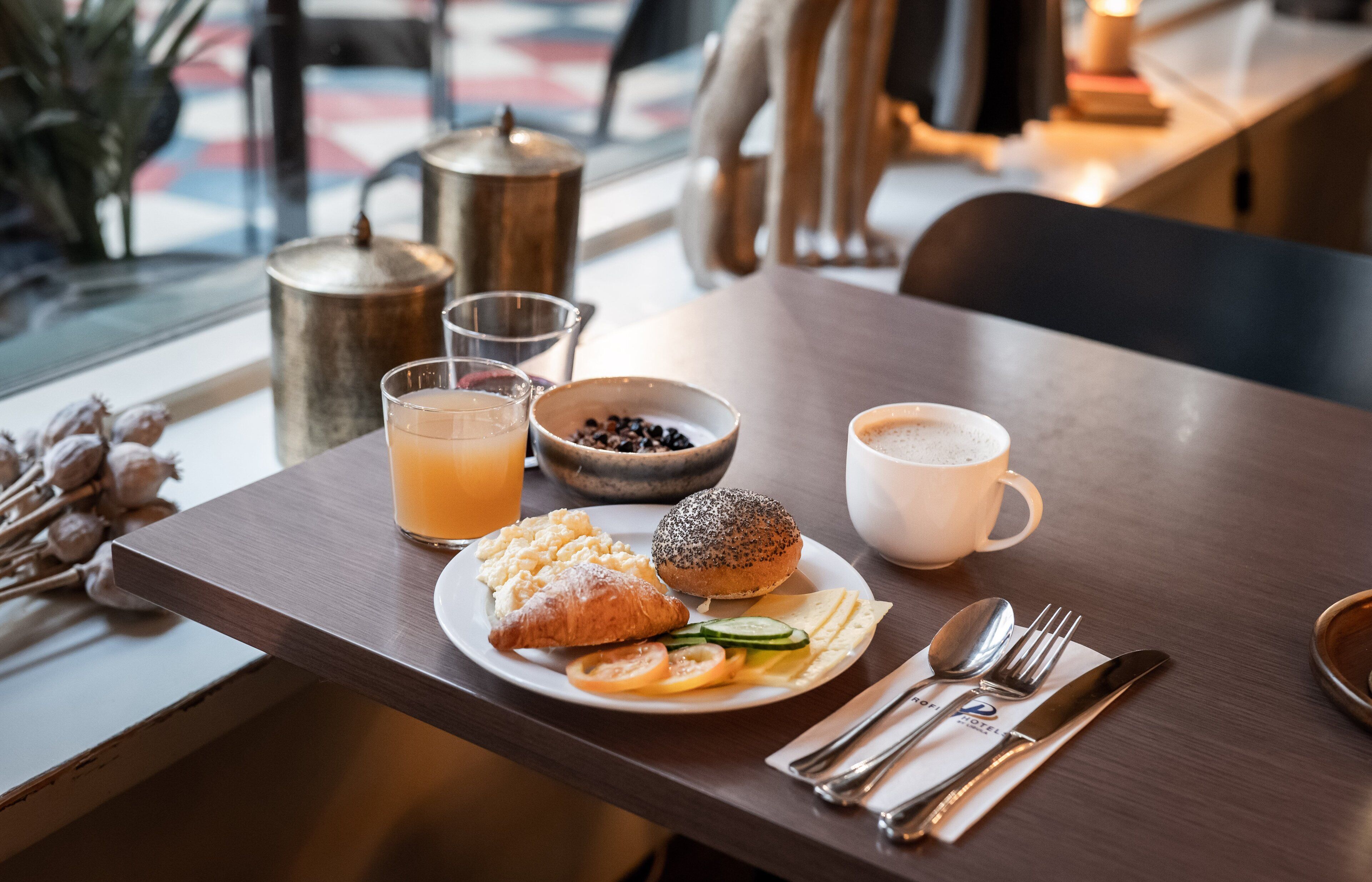 A breakfast table with a croissant, a muffin, scrambled eggs, a glass of orange juice, and a cup of coffee.