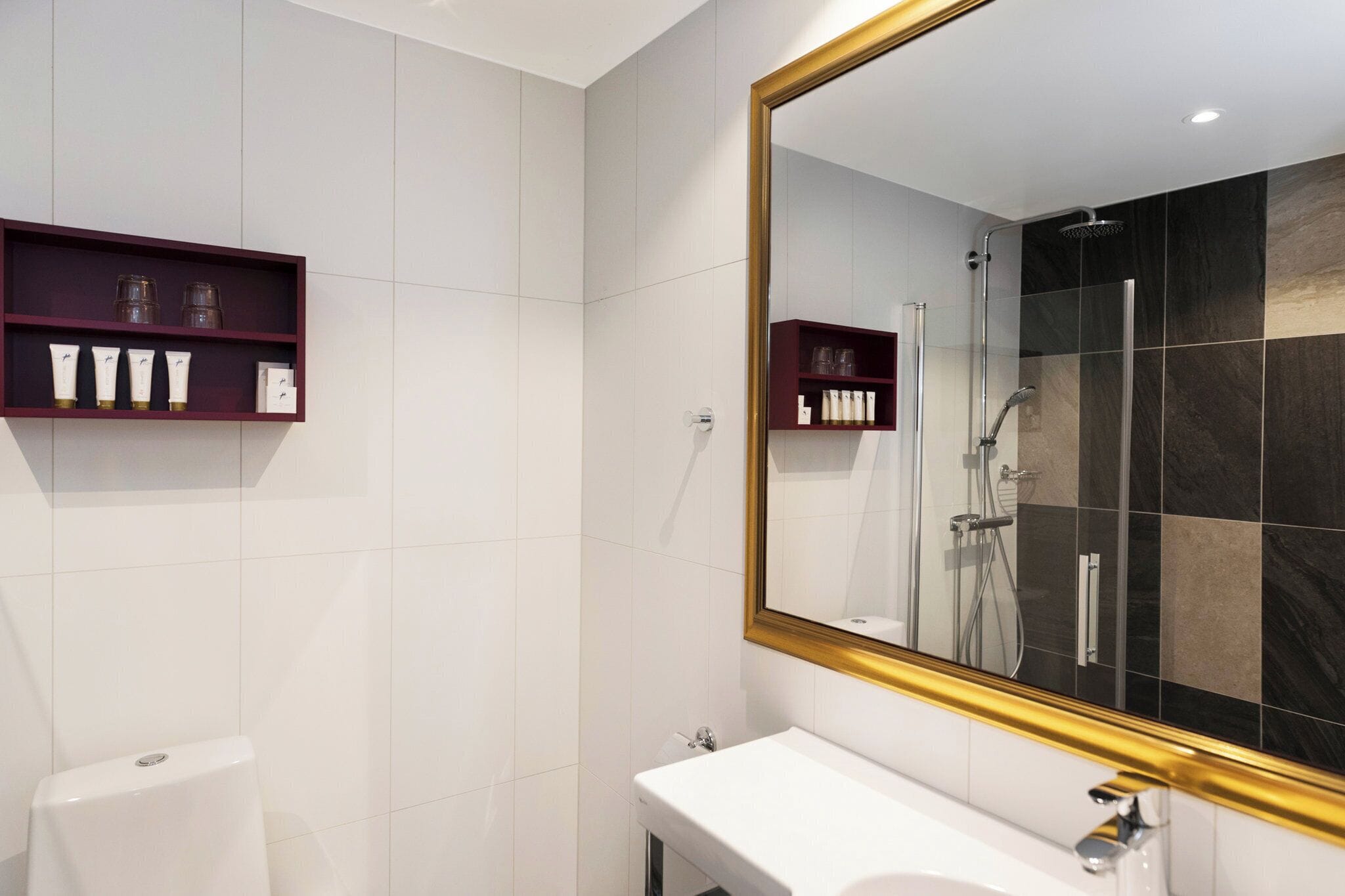 A modern bathroom with a large mirror, a shower, and a toilet.