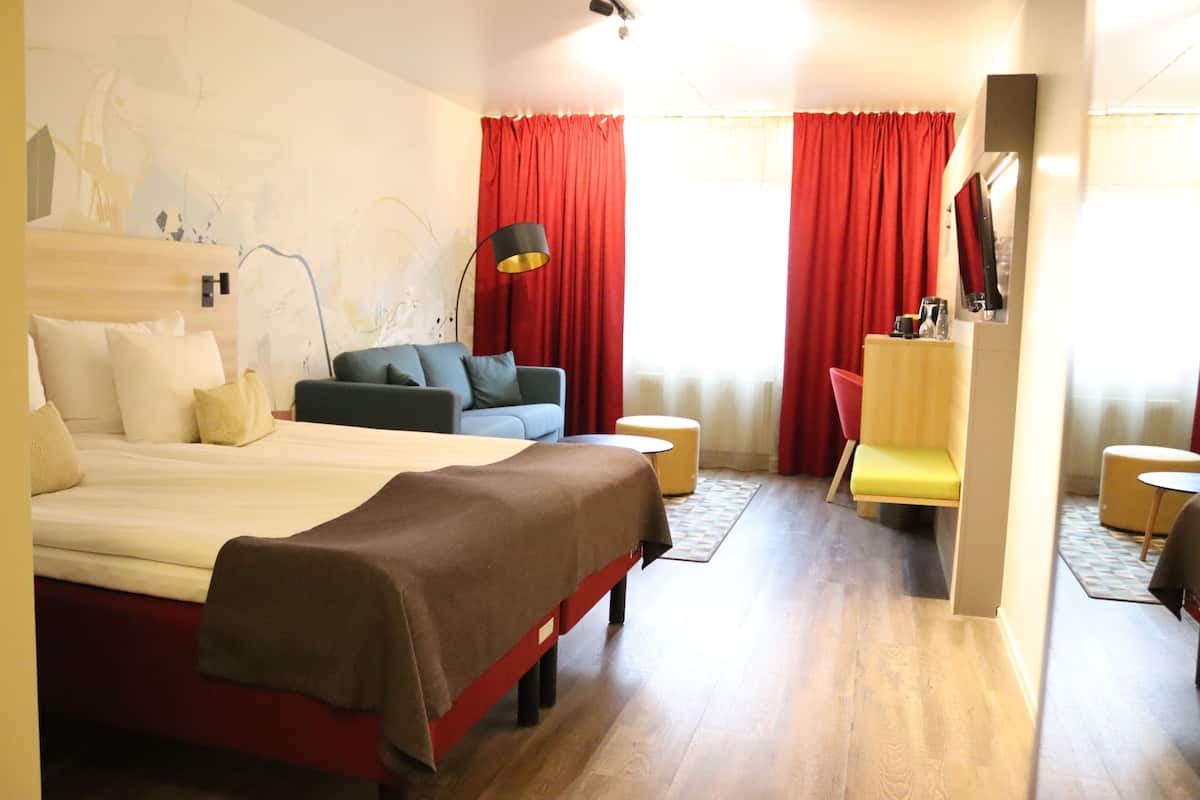 A hotel room with a bed, a sofa, a desk, and a chair.