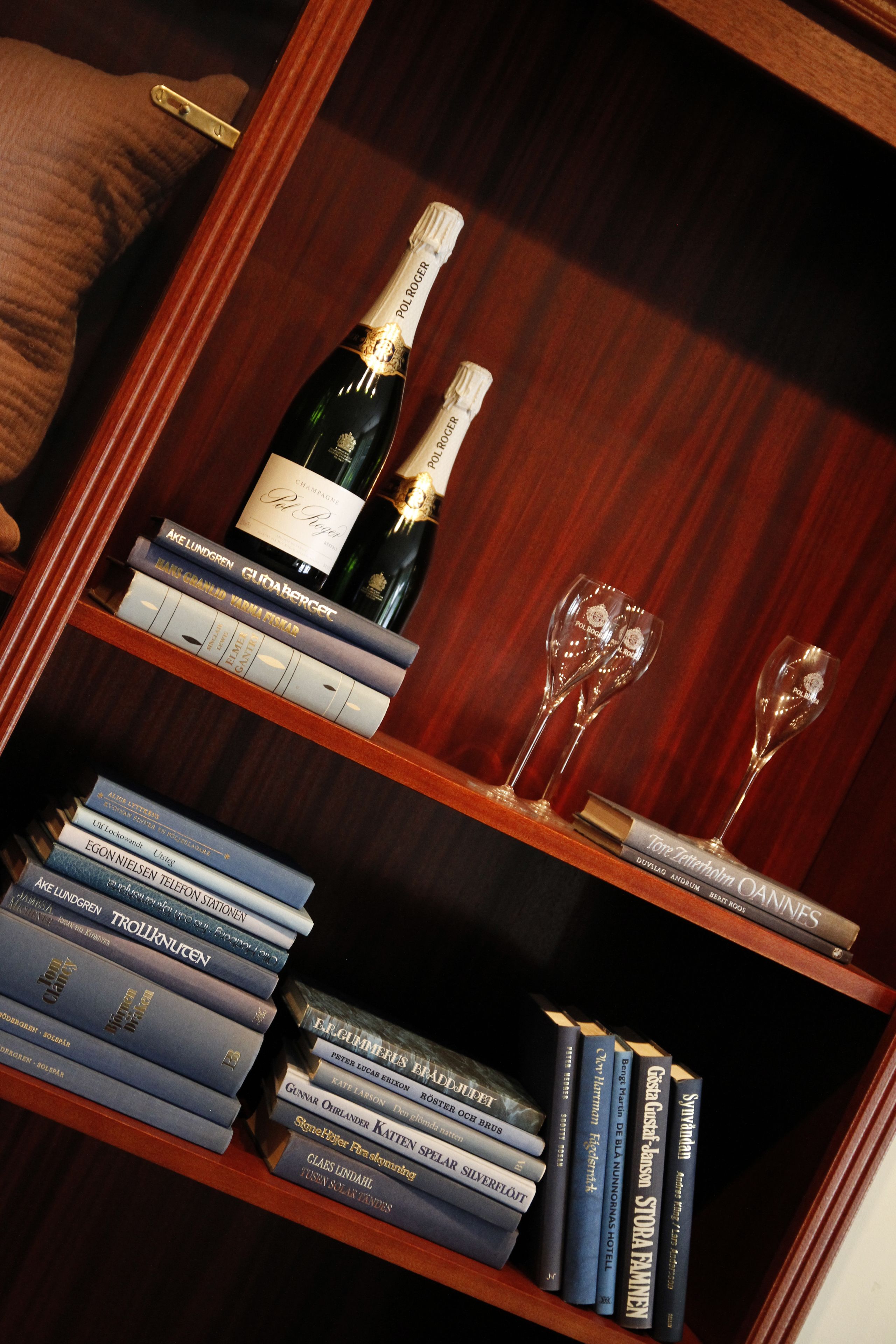 A wooden bookshelf with books and a bottle of champagne.