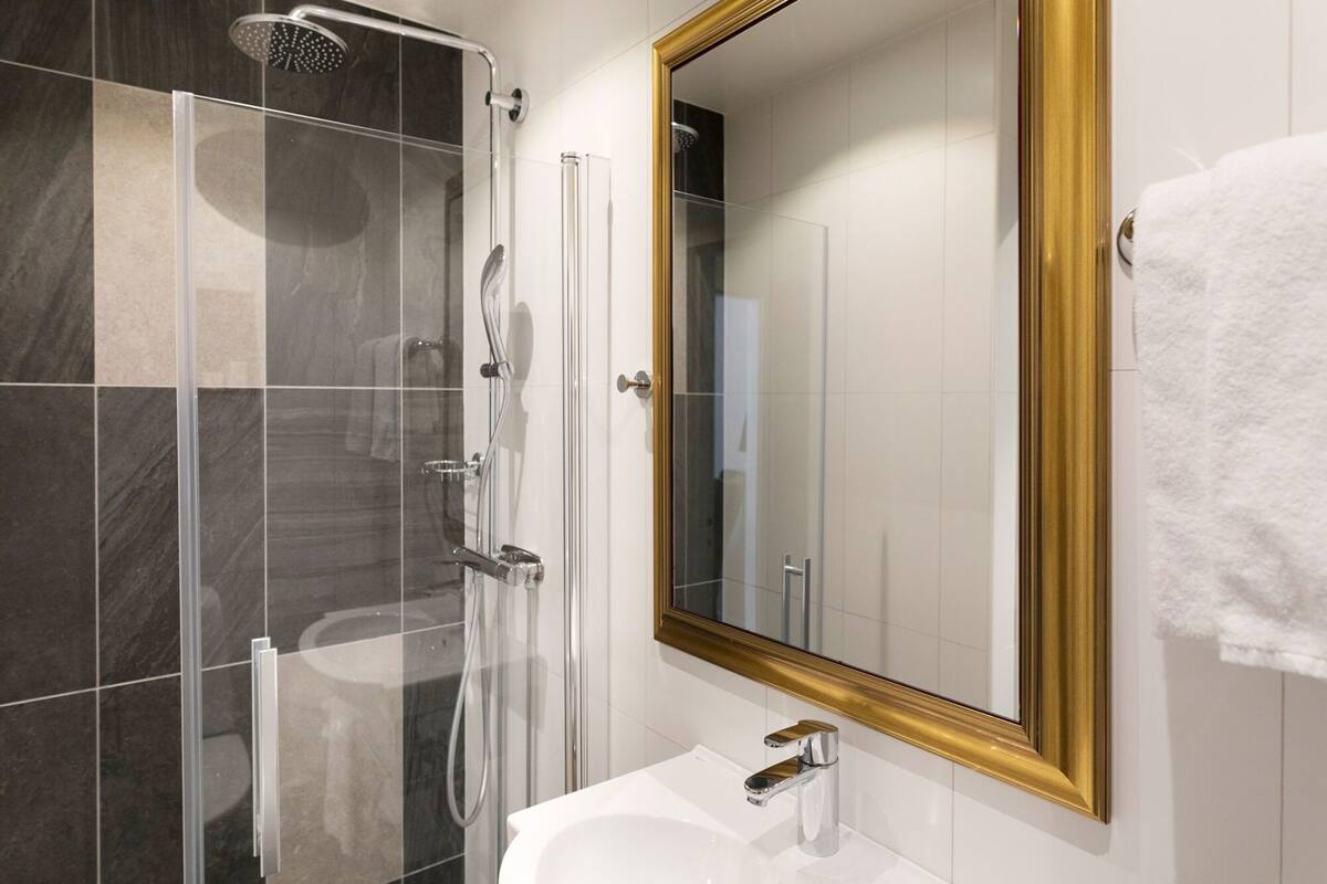 A modern bathroom with a glass shower enclosure, a white sink, and a gold-framed mirror.