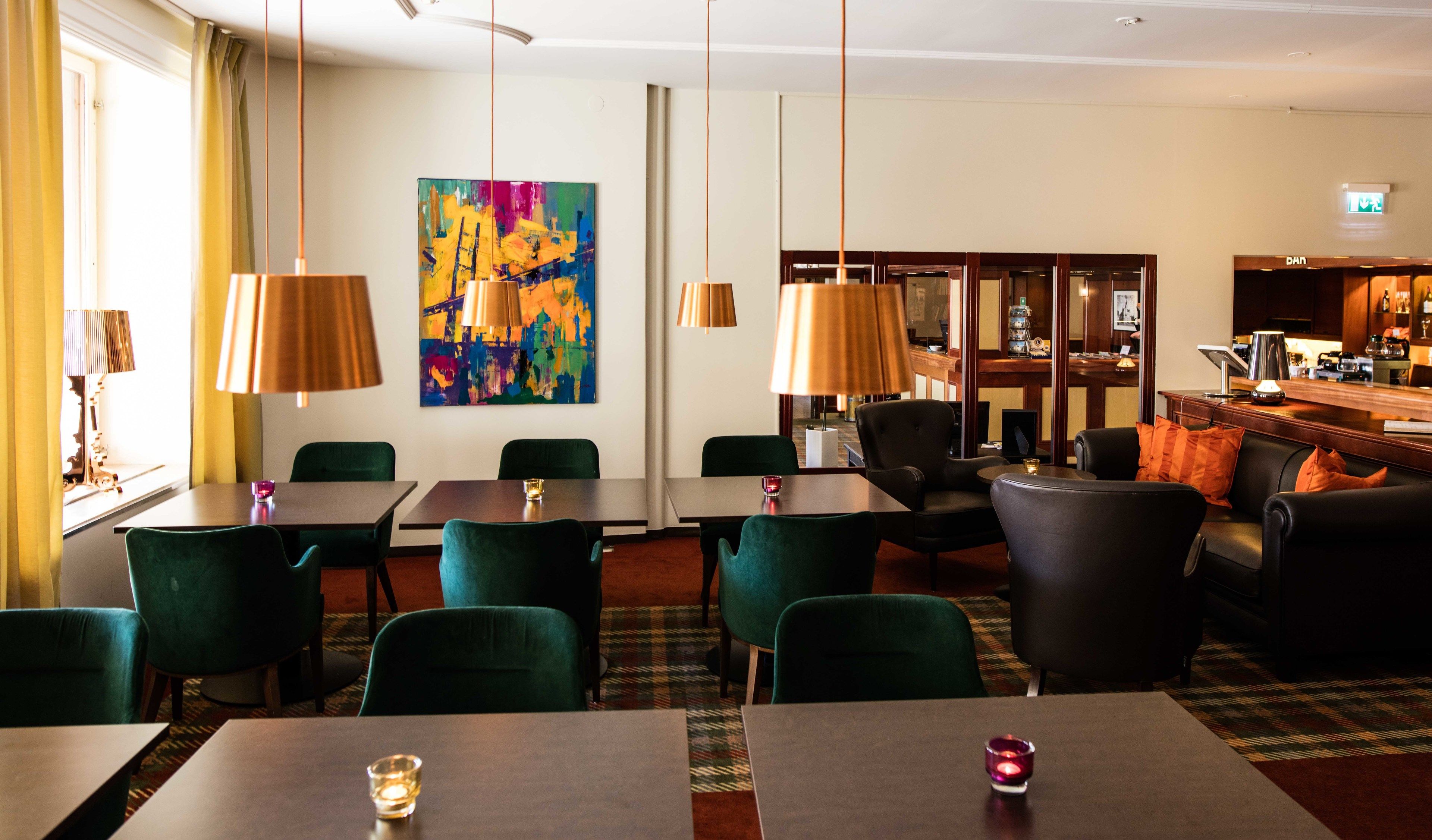 A hotel dining area with tables and chairs, a colorful abstract painting on the wall, and a bar area with a counter and stools.