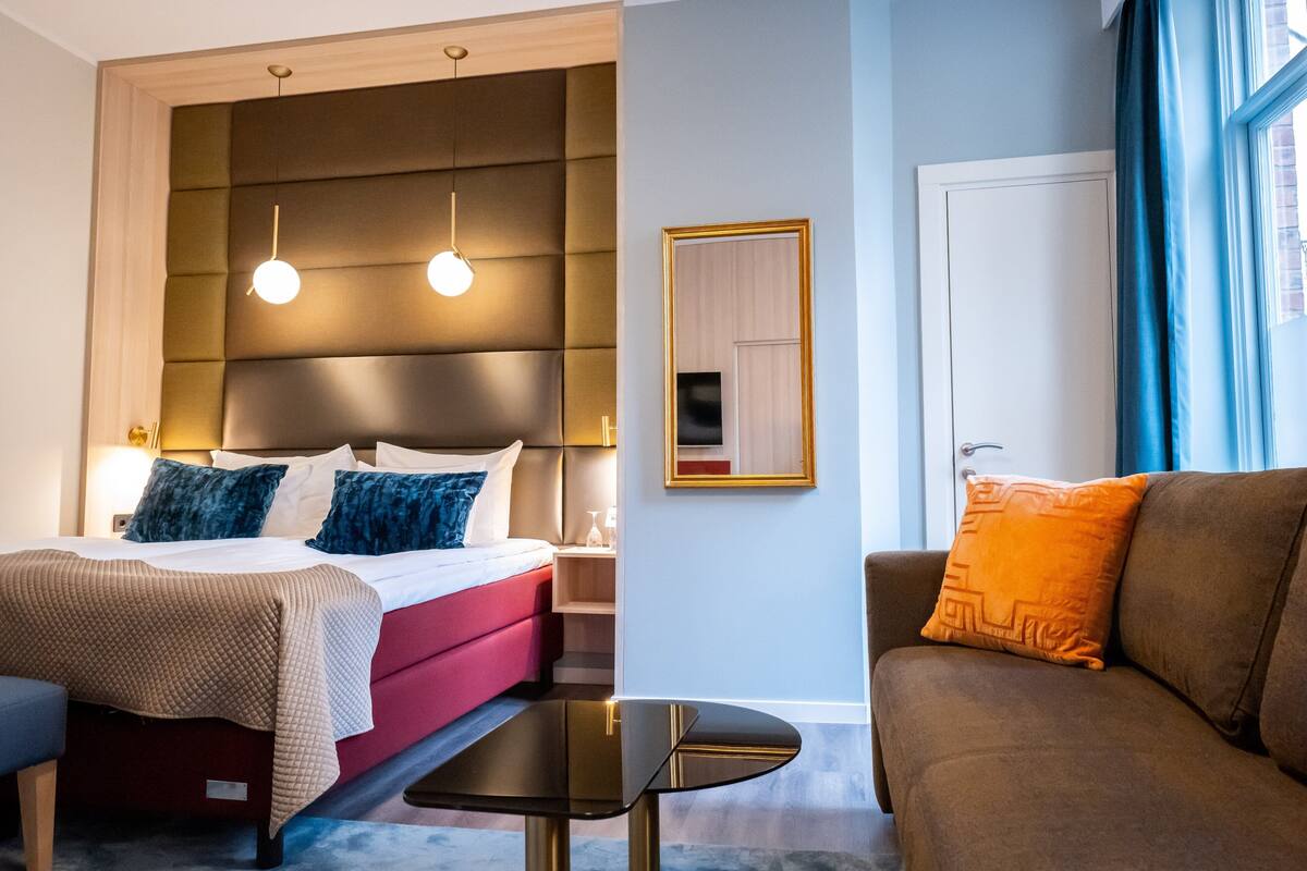 A hotel room with a bed, a sofa, a small table, and a wall-mounted TV.
