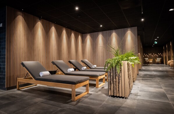 Un área de spa con paredes de paneles de madera, tres tumbonas y una maceta grande con plantas verdes.