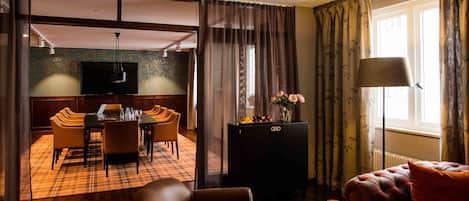 A hotel room with a dining area, a sofa, a TV, and a window with curtains.