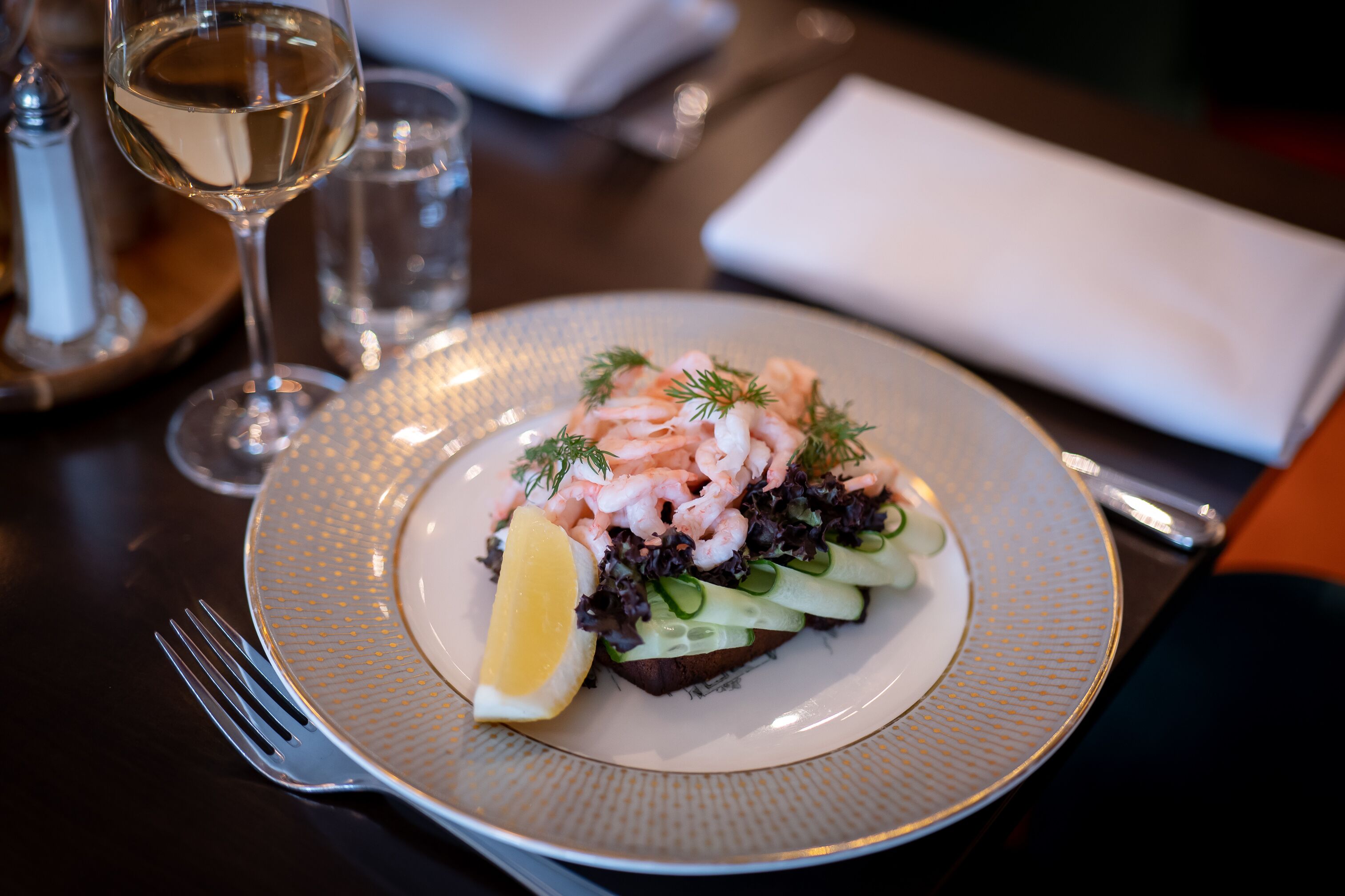 A plate of food with shrimp, vegetables, and a lemon wedge on a textured plate.