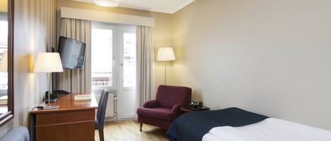 A hotel room with a bed, a desk with a computer, a chair, a TV, and a window with curtains.