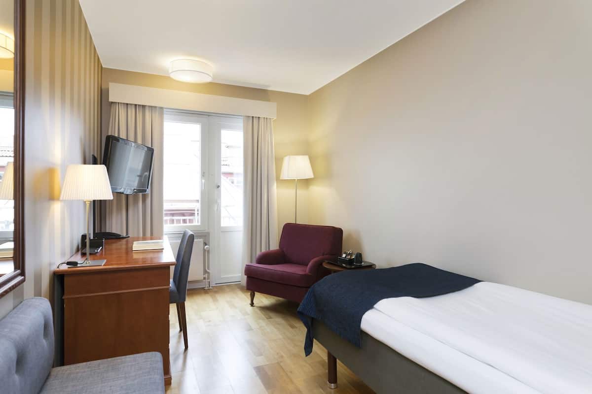 A hotel room with a bed, desk, chair, TV, and a window with curtains.
