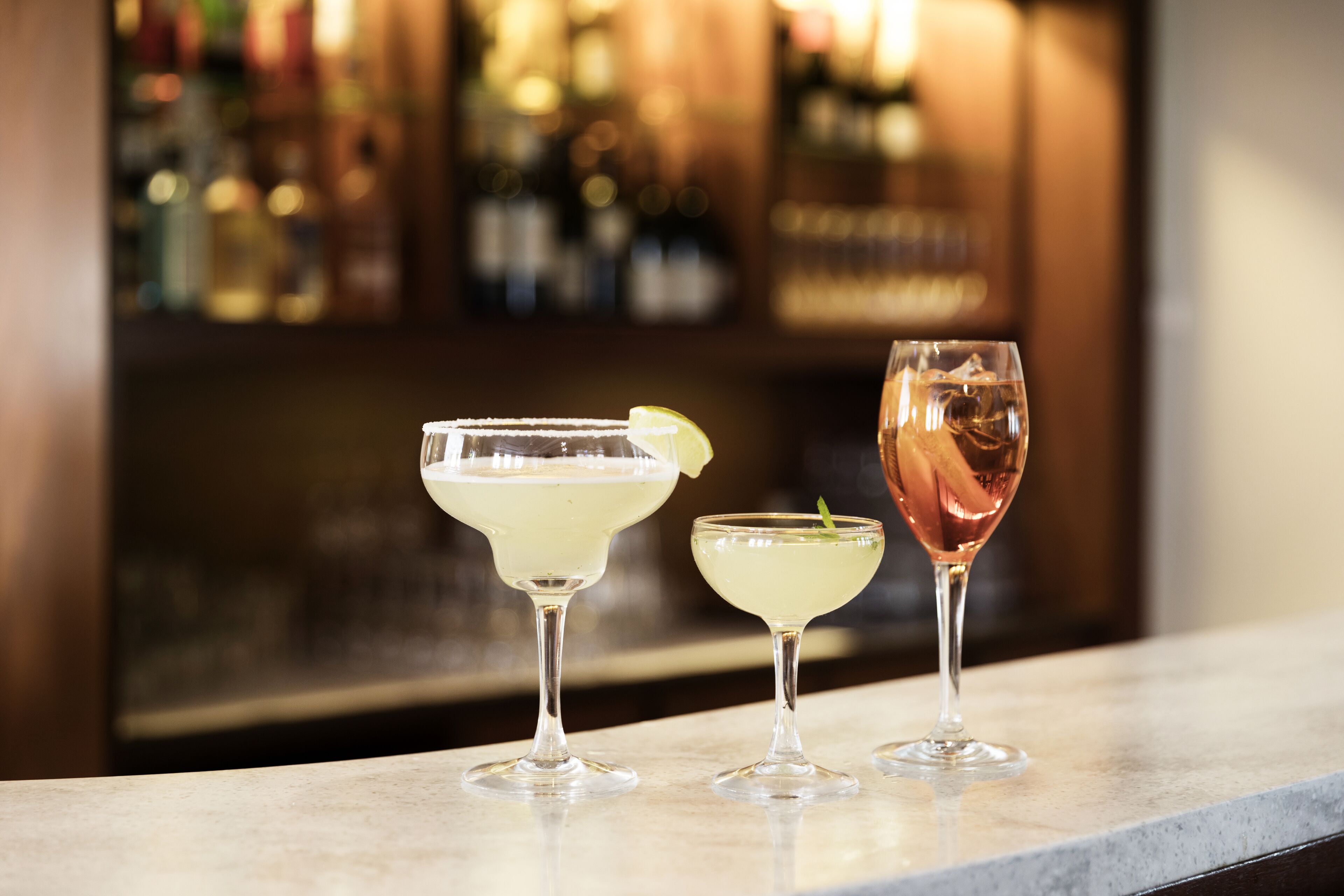Drie cocktails op een bar met een vage achtergrond van flessen.