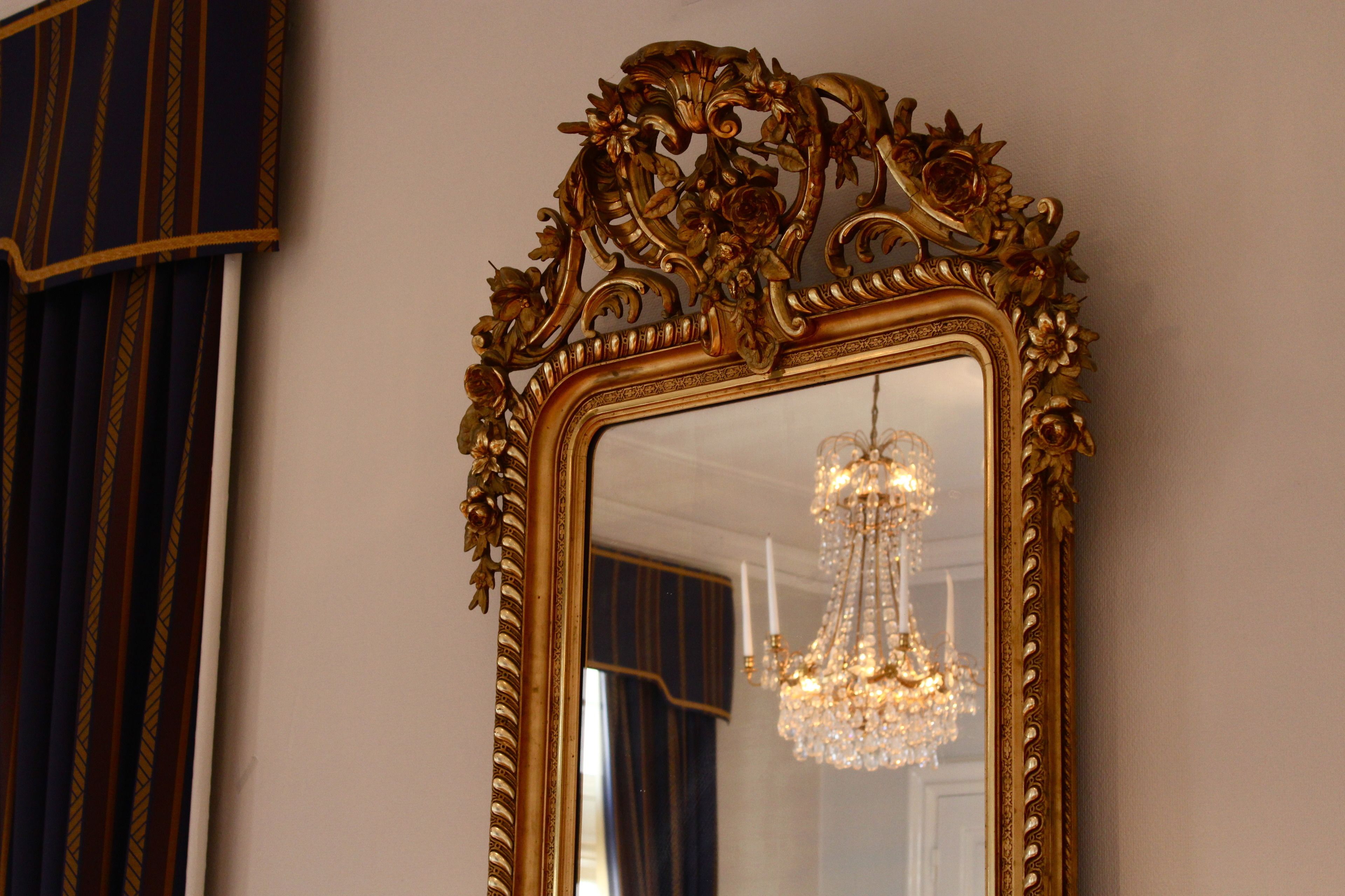 Uno specchio con una cornice dorata finemente decorata e un lampadario sullo sfondo.