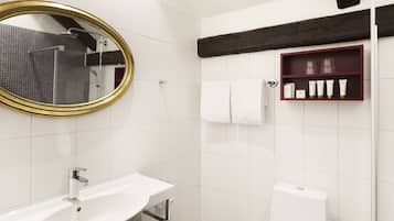A modern bathroom with a white sink, a gold-framed mirror, a shower, and a shelf with toiletries.