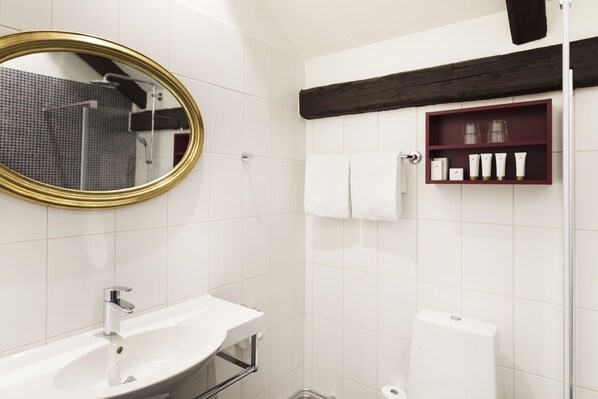 Un baño moderno con un lavamanos blanco, un espejo con marco dorado, una ducha y un estante con artículos de aseo.