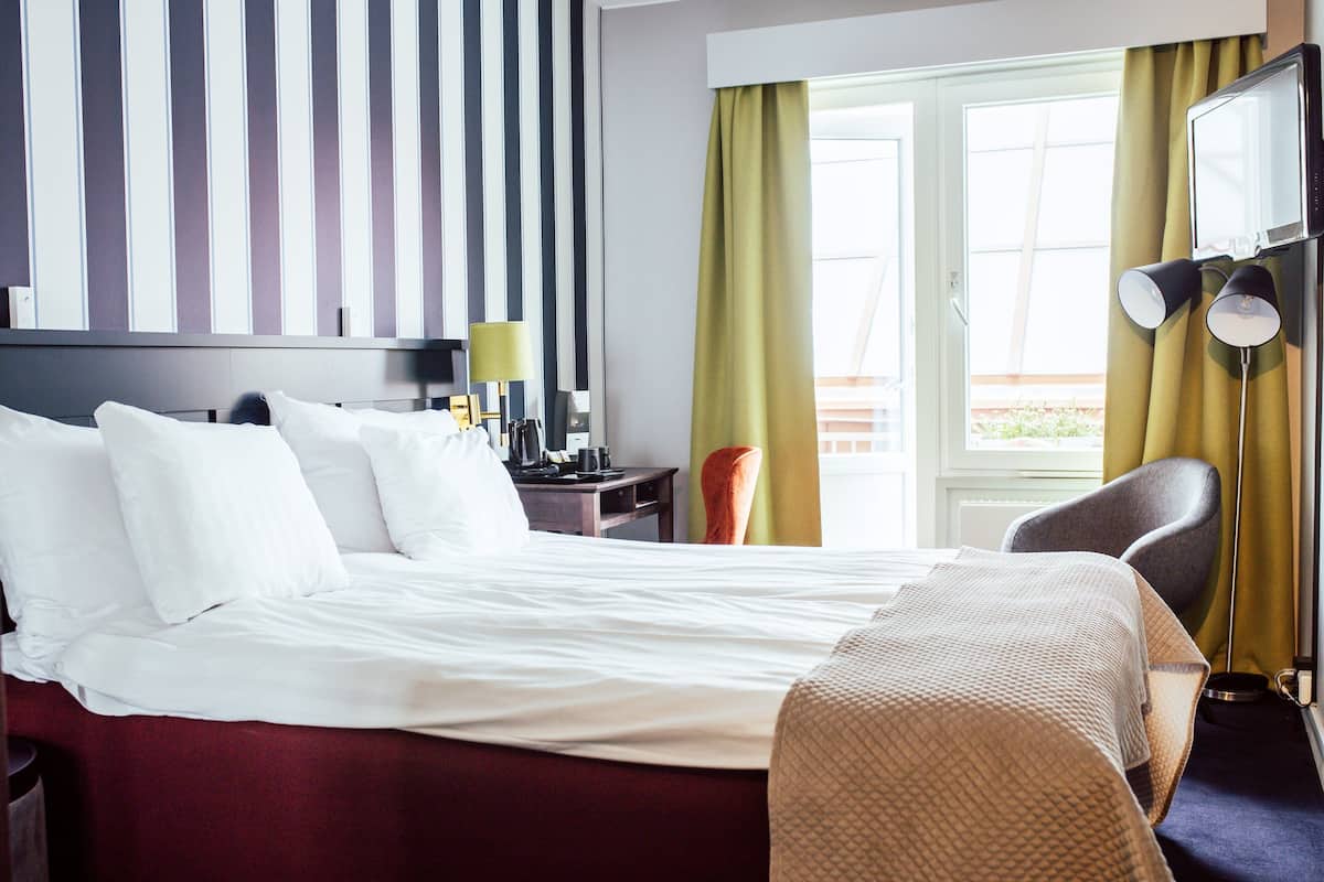A hotel room with a large bed, a desk with a lamp, a chair, and a television mounted on the wall.
