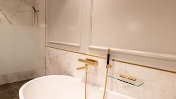 Ein modernes Badezimmer mit freistehender Badewanne, goldenen Armaturen und Marmorwänden.