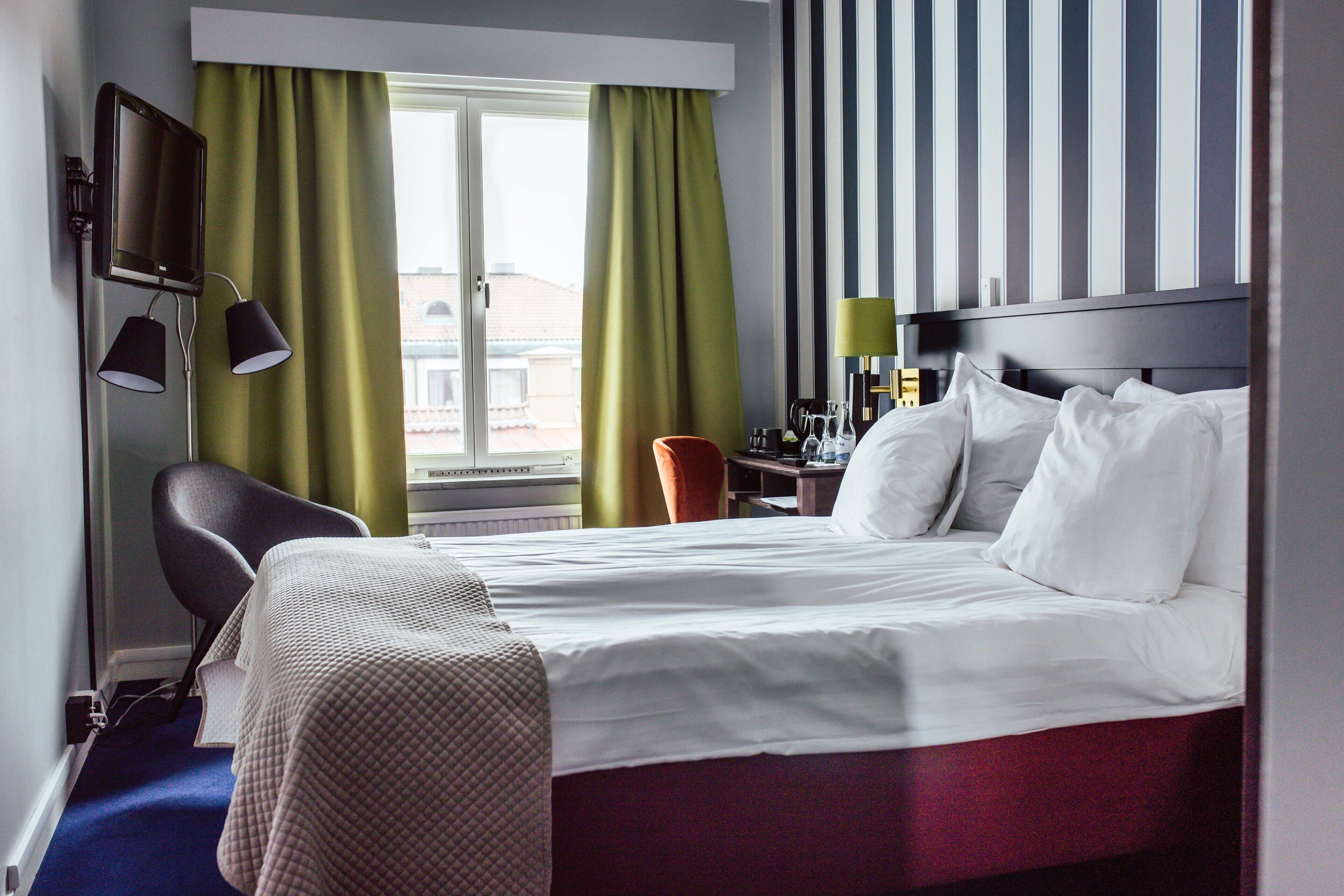Una habitación de hotel con cama, escritorio, silla, televisor y cortinas.