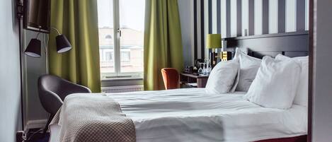 A hotel room with a bed, a desk, a chair, a TV, and curtains.