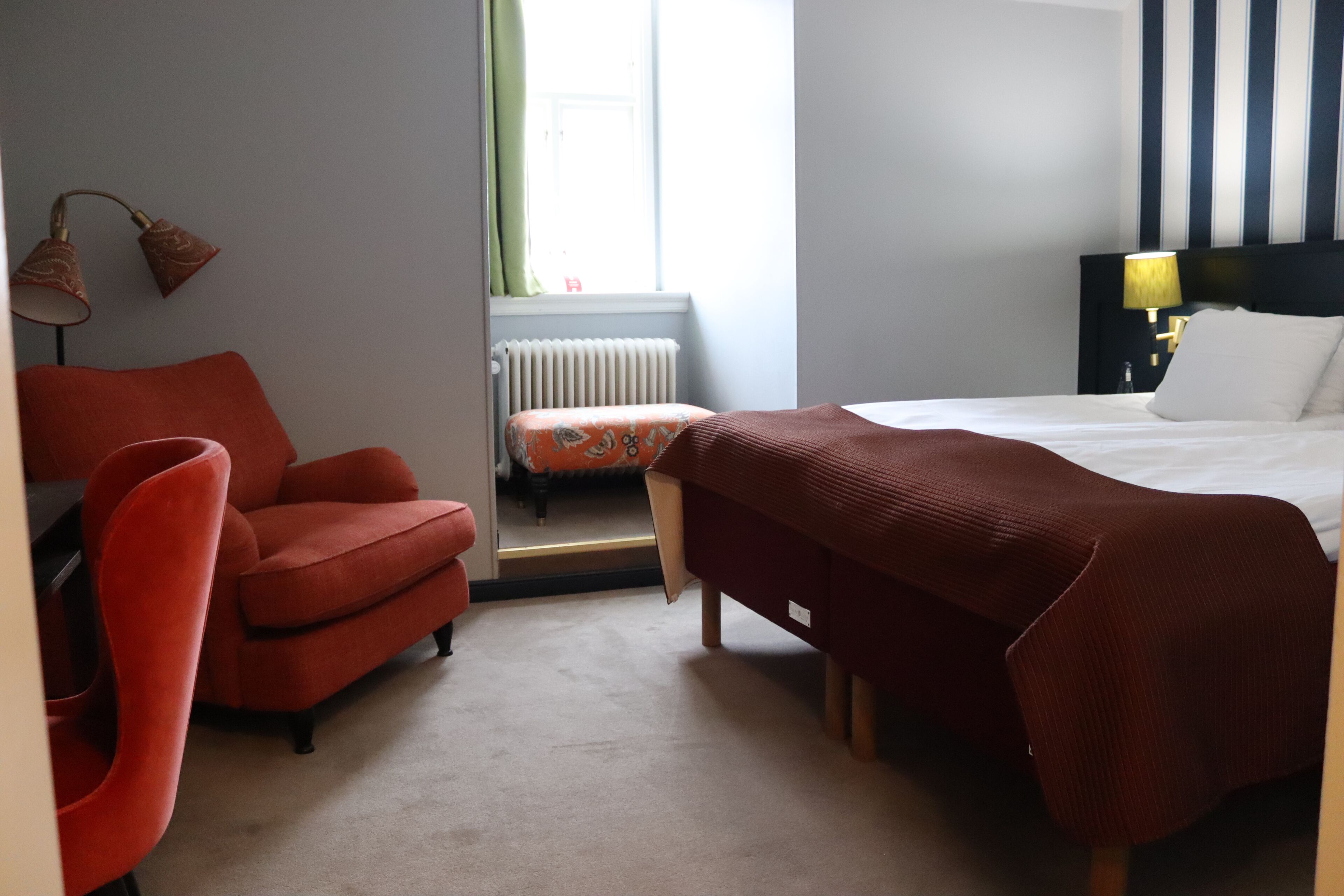 Een hotelkamer met een bed, een rode fauteuil, een klein tafeltje en een lamp.