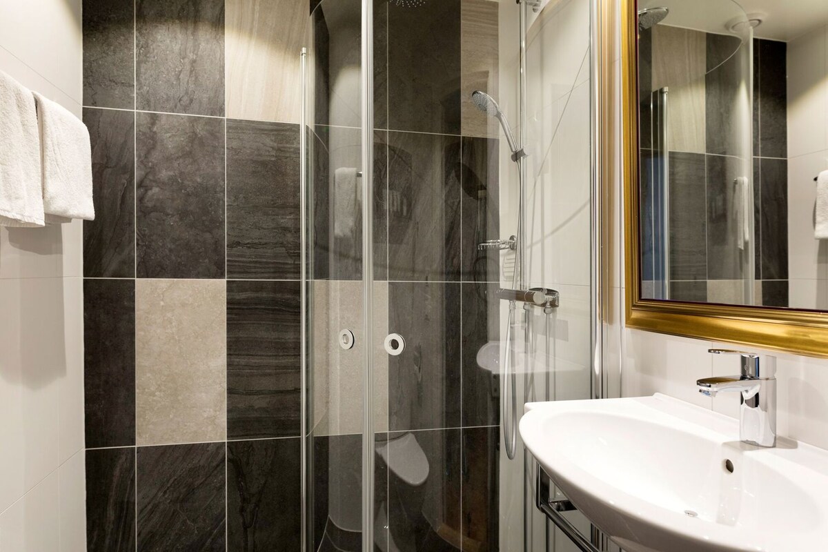 A modern bathroom with a glass shower enclosure, a white sink, and a large mirror with a gold frame.