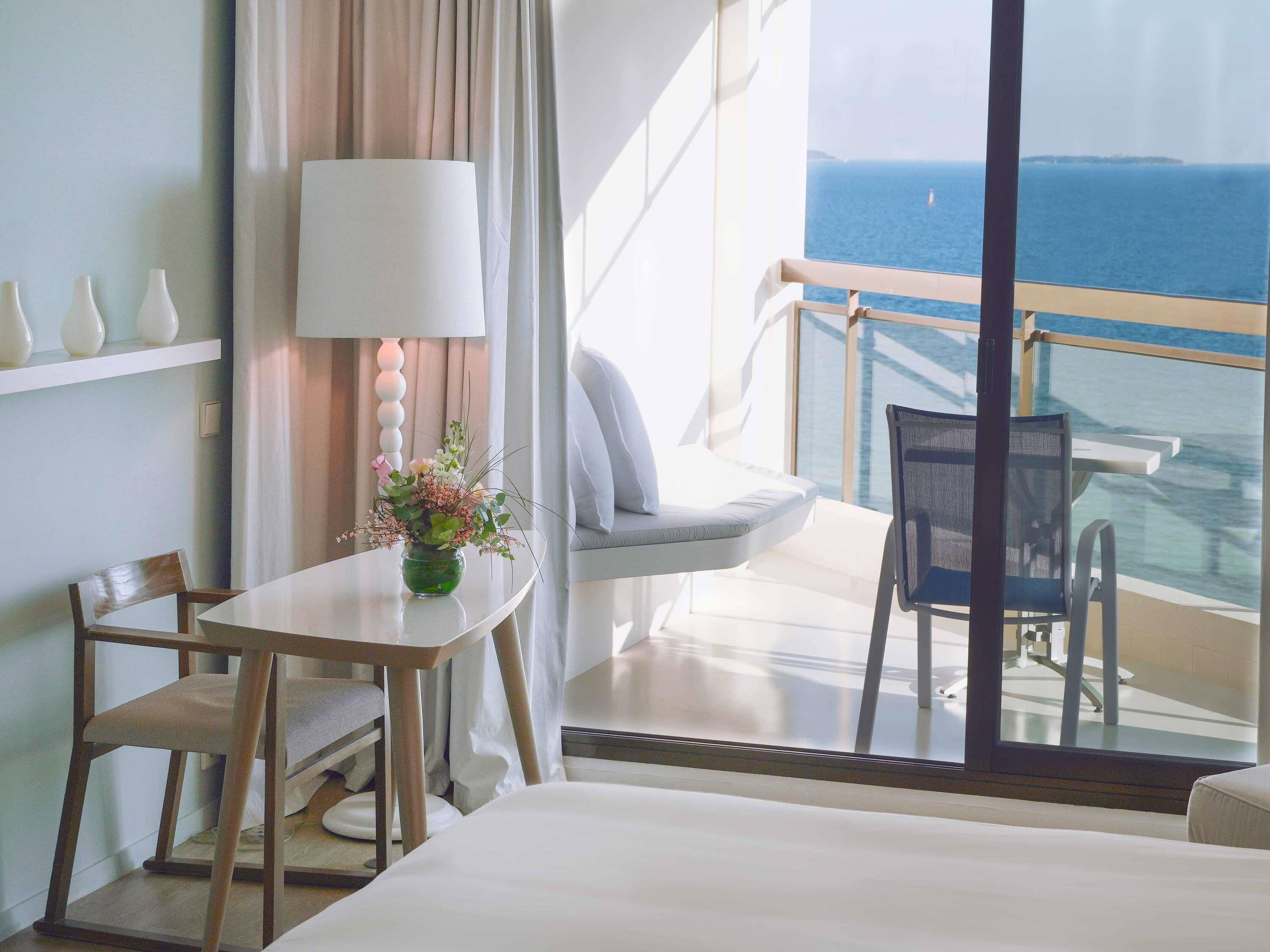 Une chambre d’hôtel avec un balcon, une table à manger, une chaise, un canapé et un lit.