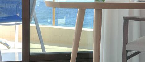 A room with a view of the sea, a table with a vase of flowers, and a chair.