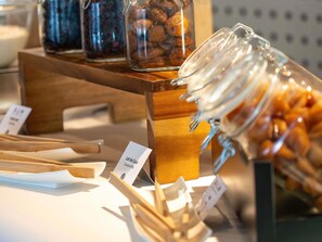 Una exhibición de frascos con diversos alimentos, incluyendo aparentemente leche de coco, sobre un soporte de madera con etiquetas de precio.
