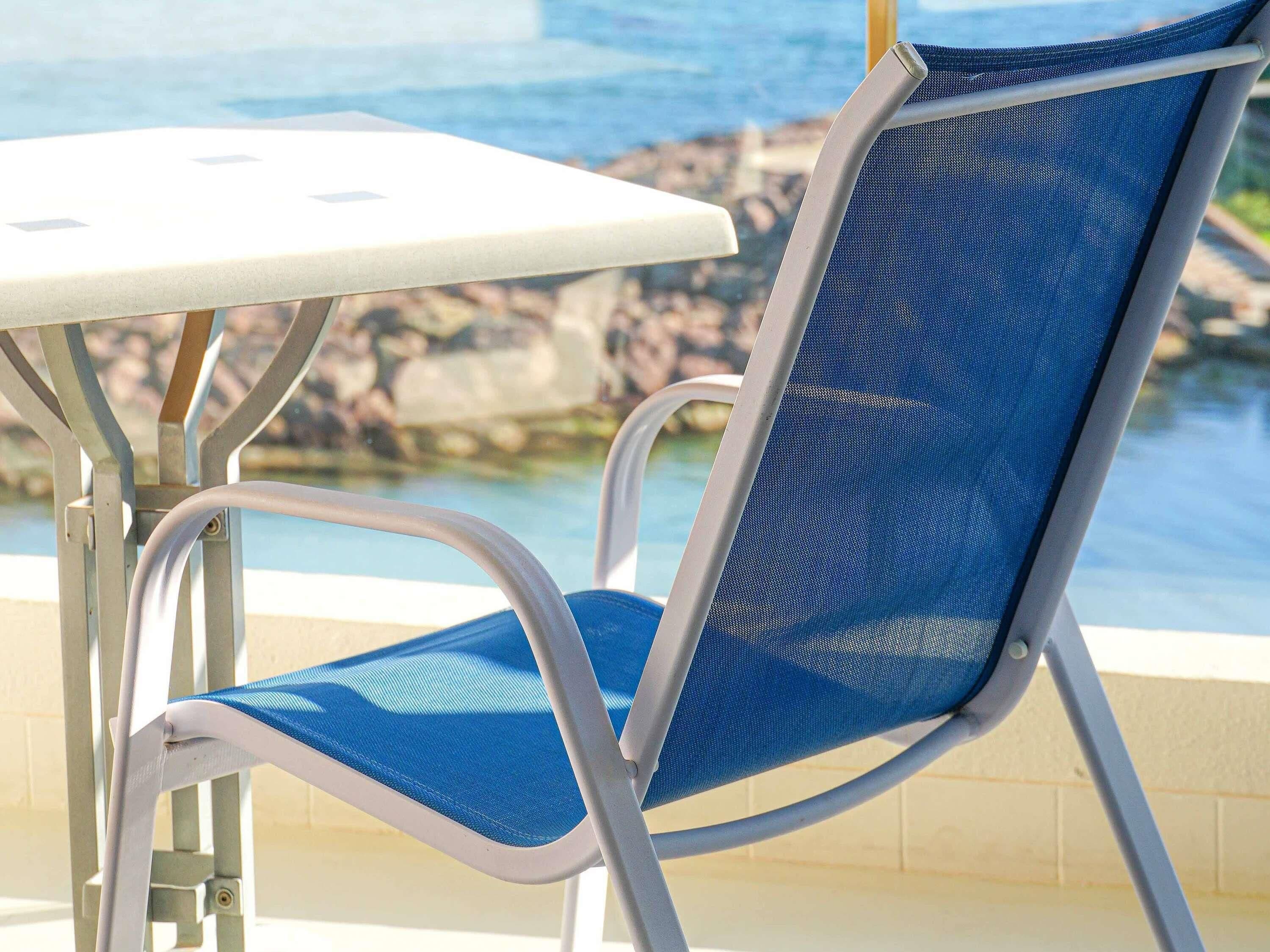 Une chaise avec un dossier en tissu ajouré et une table à la surface blanche, placées près du bord d’une piscine.