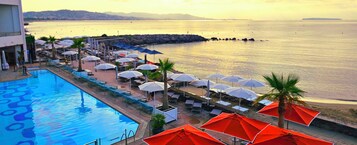 Zona de piscina con sombrillas y sillones reclinables, vista despejada al mar y un rompeolas rocoso al fondo.