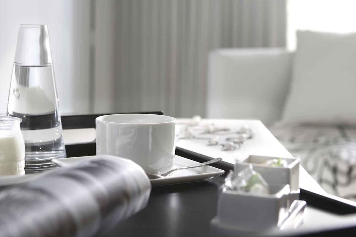 A modern hotel room with a dining area featuring a tray with a glass of water, a white mug, and a small bowl of food.