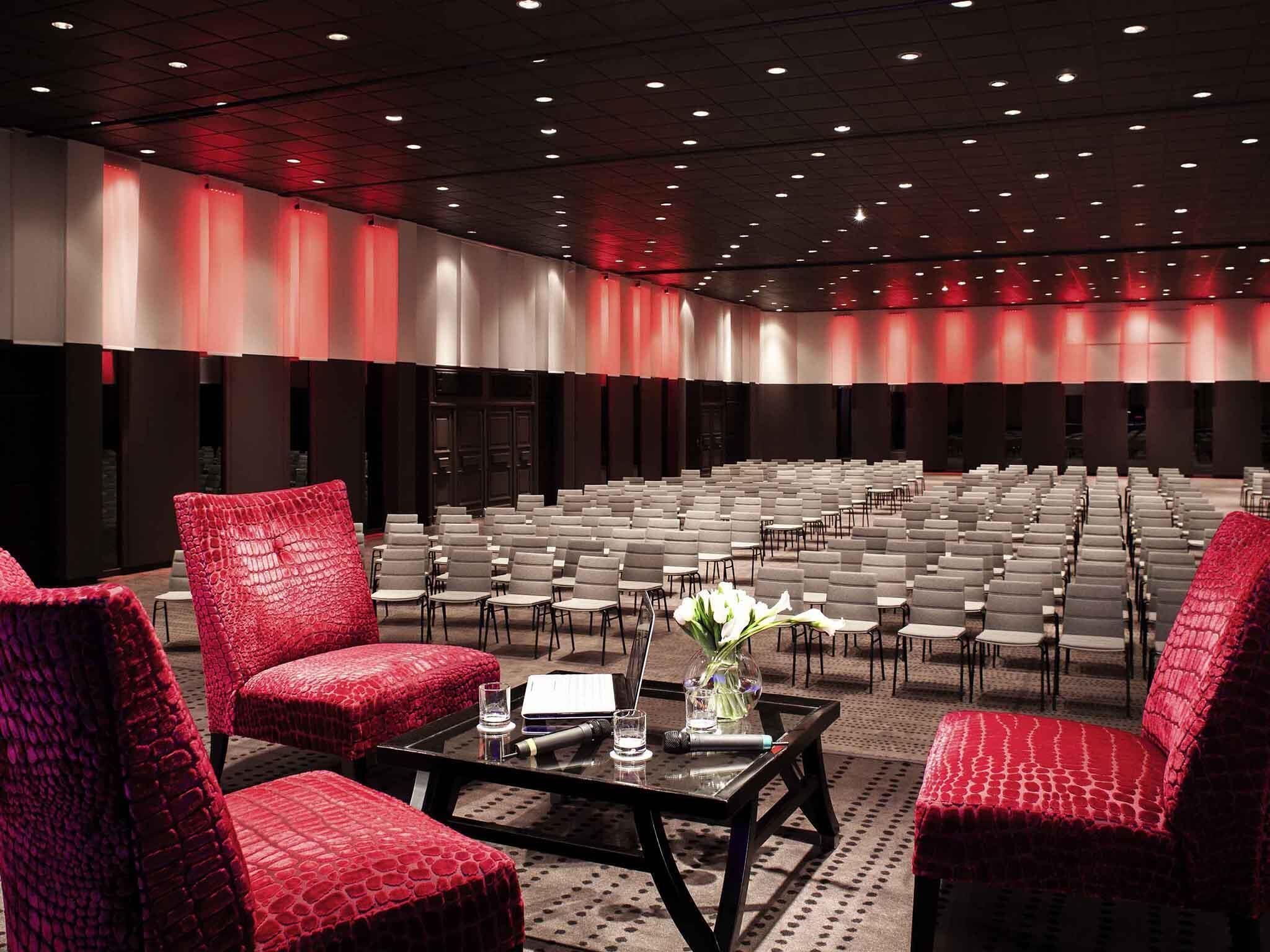 A conference room with rows of chairs, a stage, and red upholstered chairs.