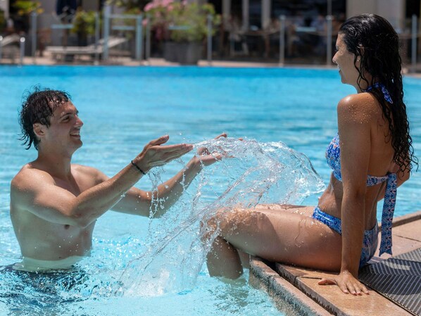 A pool with clear water, a person sitting on the edge, and another person reaching out.