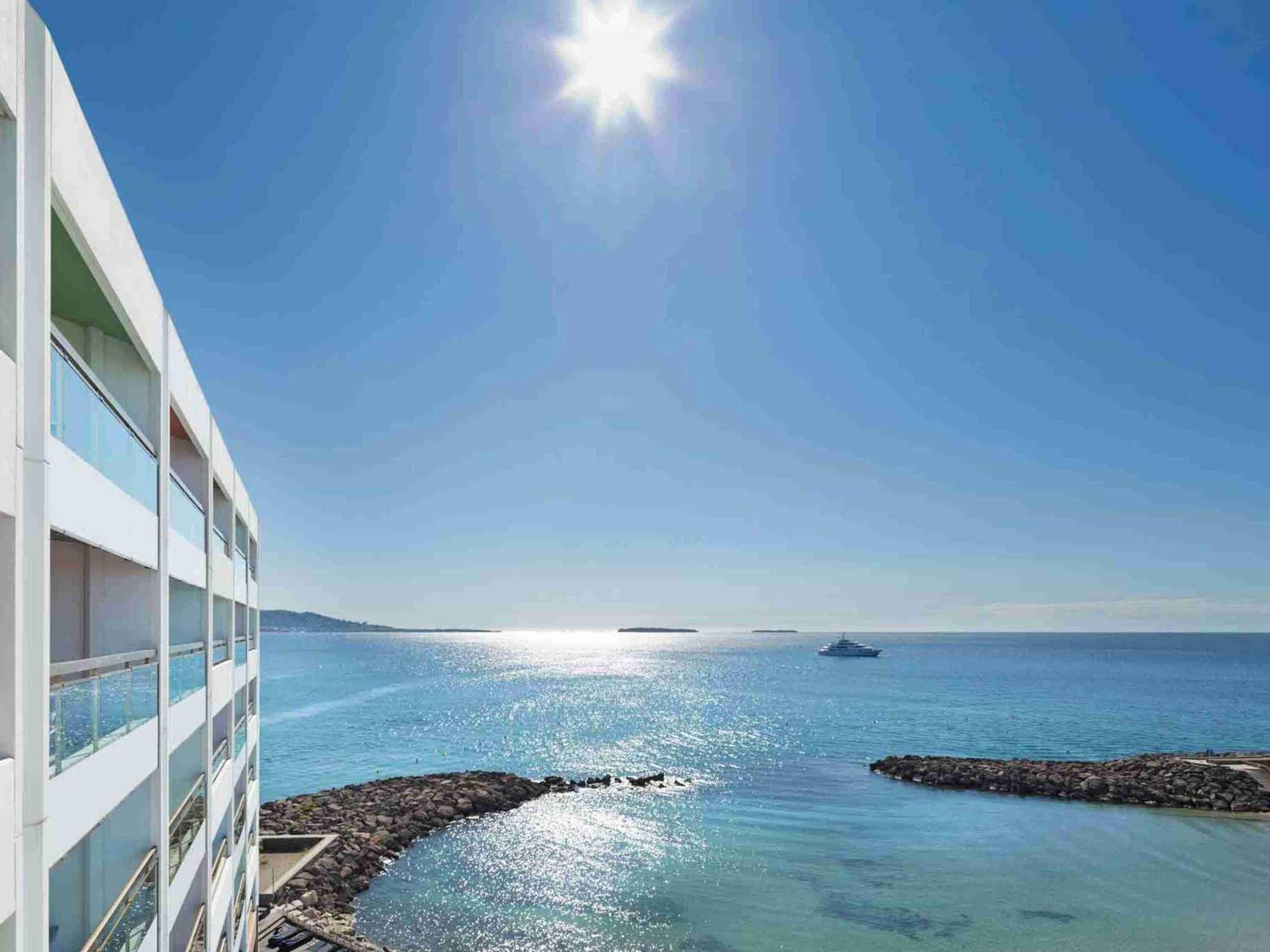 A modern building with large windows overlooking a calm sea and a clear sky.