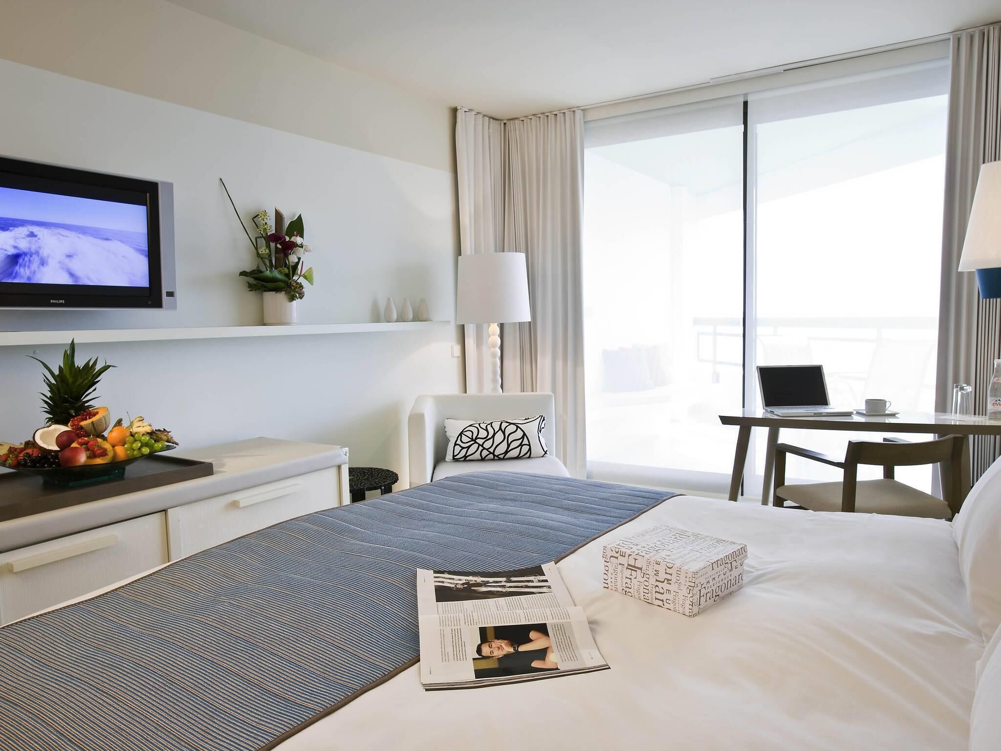 A hotel room with a bed, a desk with a laptop, a television, and a window with curtains.