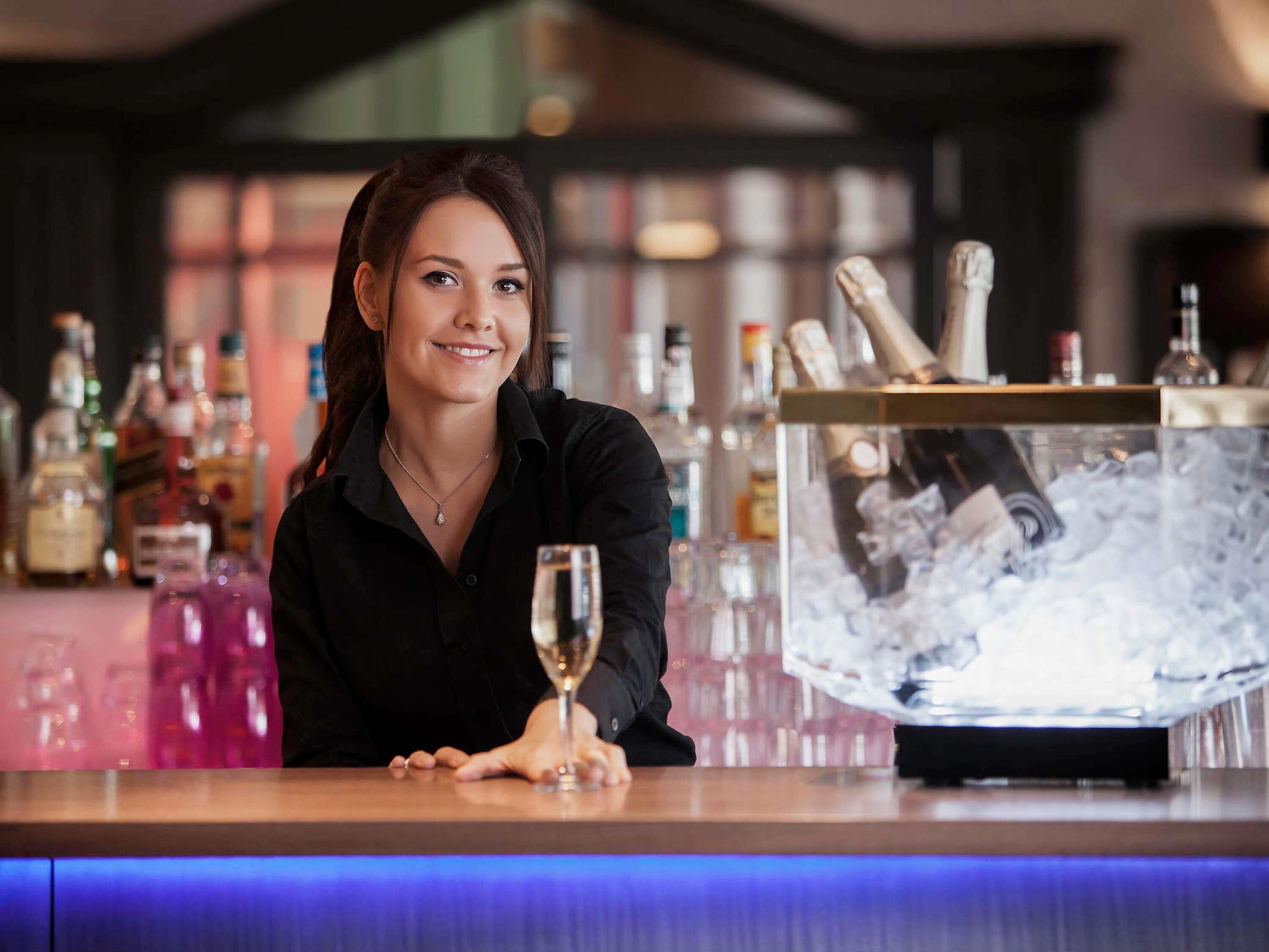 Un espace bar avec un barman, un grand seau à glace et diverses bouteilles de spiritueux.